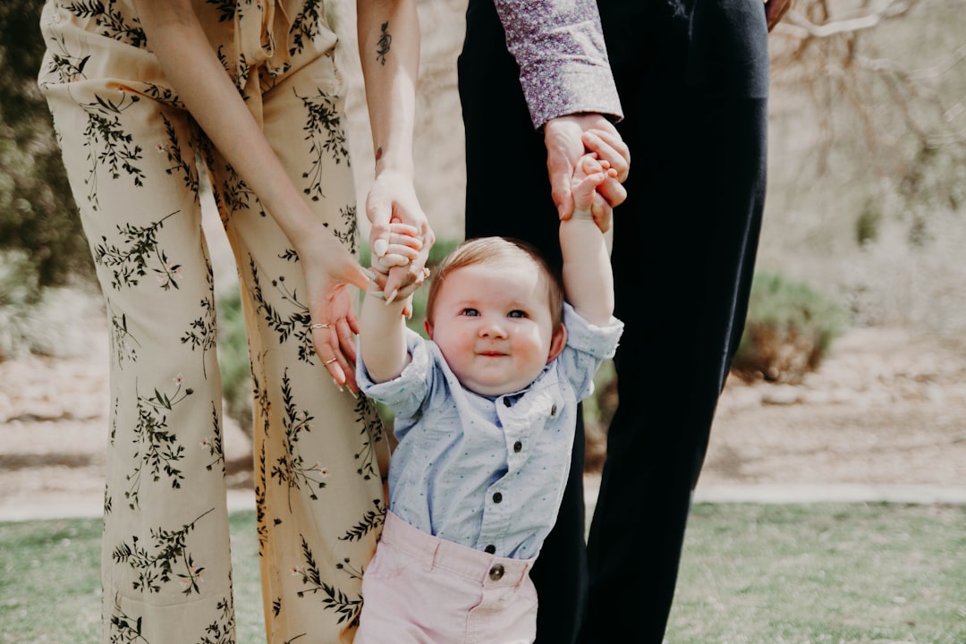 man and woman holding hand of toddler walking on grass field, family photo