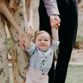 man and woman holding hand of toddler walking on grass field