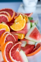 Close-up of sliced fruits—pineapple, lemon, and mango—arranged artistically on a white surface.