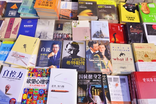 A variety of books are displayed on a table. The collection includes titles in both English and Chinese, and covers multiple genres. Prominent cover images include a man in a suit, a classic film scene, and abstract artwork. Many of the books have bright, colorful covers, while others are more muted.