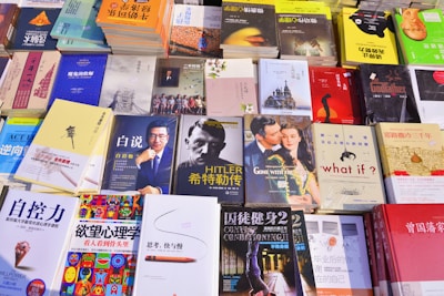 A variety of books are displayed on a table. The collection includes titles in both English and Chinese, and covers multiple genres. Prominent cover images include a man in a suit, a classic film scene, and abstract artwork. Many of the books have bright, colorful covers, while others are more muted.