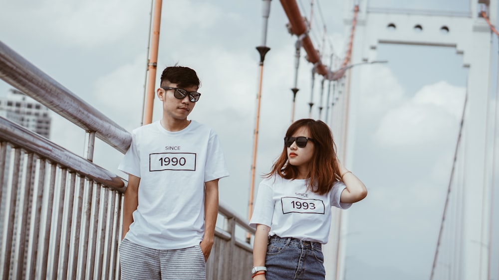 man and woman standing beside gray rails on bridge during daytime