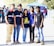 A diverse group of people wearing casual dark-themed clothing, smiling outdoors.