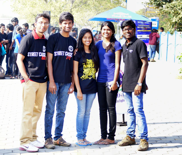 A group of smiling classmates proudly wearing their custom anniversary t-shirts in a sunny park.
