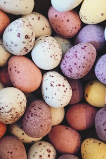 A pile of small, speckled candy eggs in a variety of pastel colors including pink, purple, yellow, and off-white.