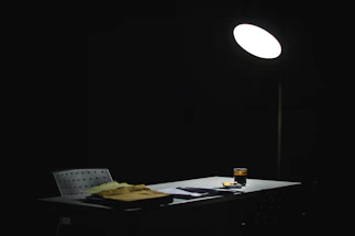 A dimly lit desk with scattered case files and a flickering red lamp casting shadows.