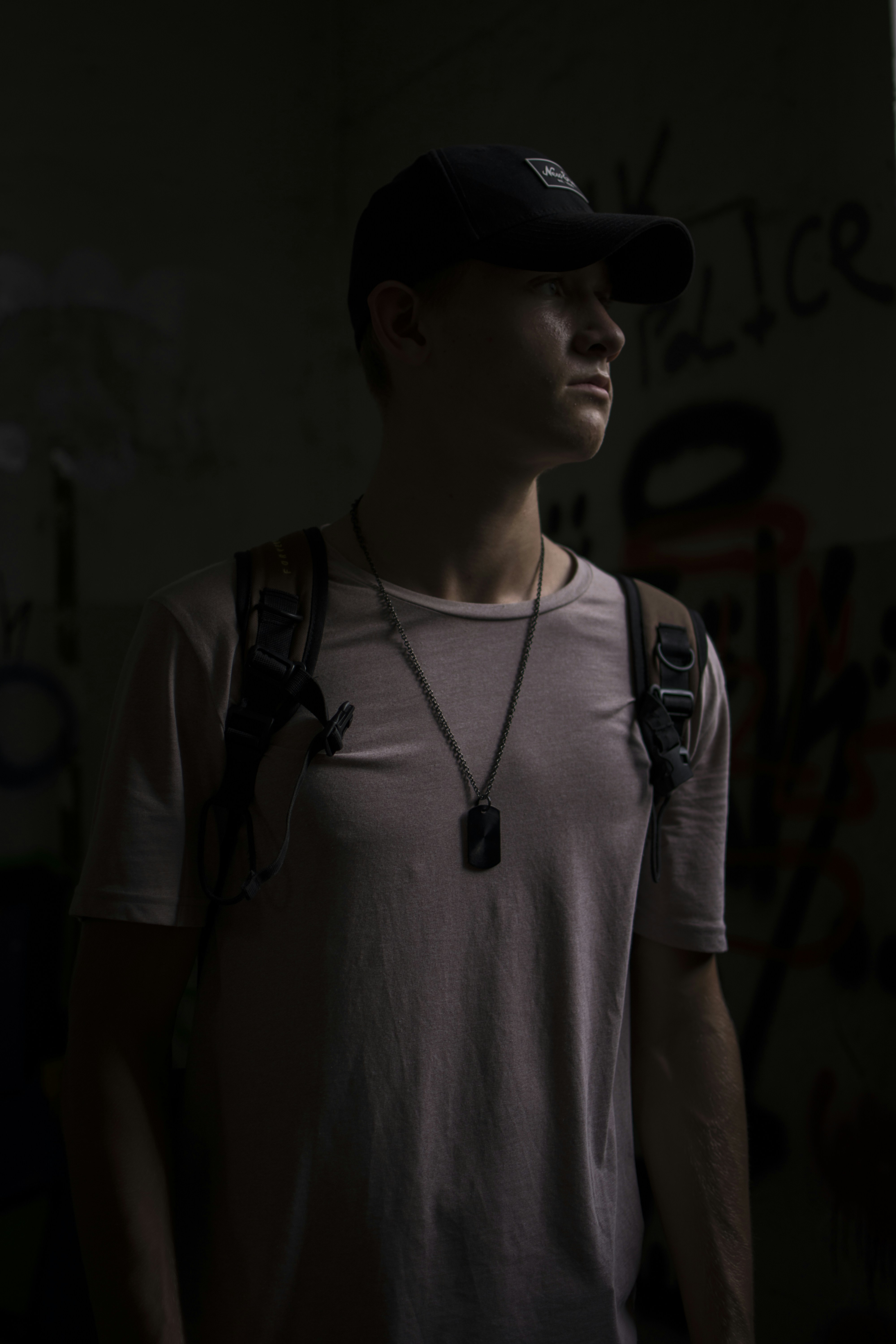 homme portant un T-shirt blanc et un sac à dos debout dans une pièce sombre éclairée