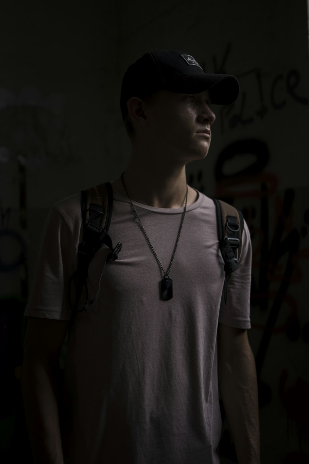 man wearing white T-shirt and backpack standing in a dark lit room