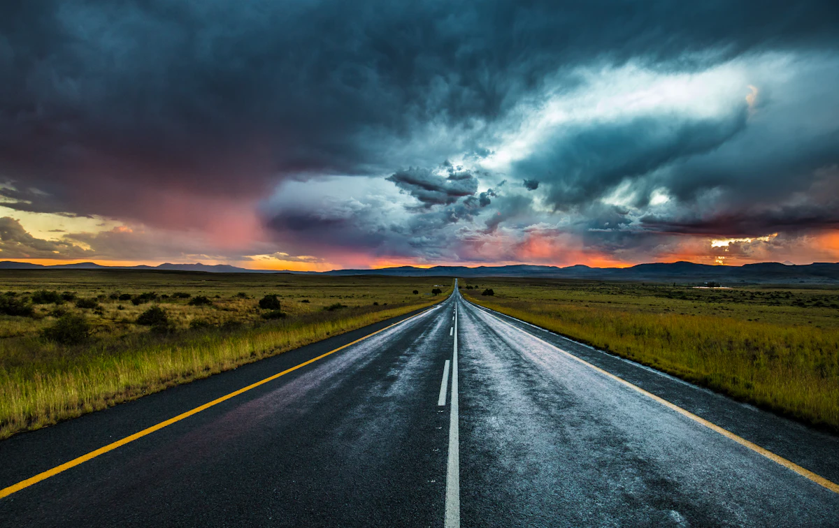 A paved road running straight to the horizon under storm clouds at sunset near Nieu-Bethesda