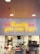 Neon sign in yellow text reading 'Quality you can taste' is mounted on a white tiled wall inside a fast food restaurant. Beneath the sign, several workers dressed in white uniforms and red hats are busy at a counter preparing food.