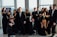 Smiling diverse group of people wearing casual and elegant outfits in a bright, modern setting.
