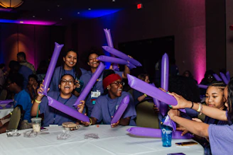 A vibrant group of diverse community members smiling and working together in a bright, purple-themed learning center.