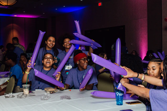 A vibrant group of diverse community members smiling and working together in a bright, purple-themed learning center.