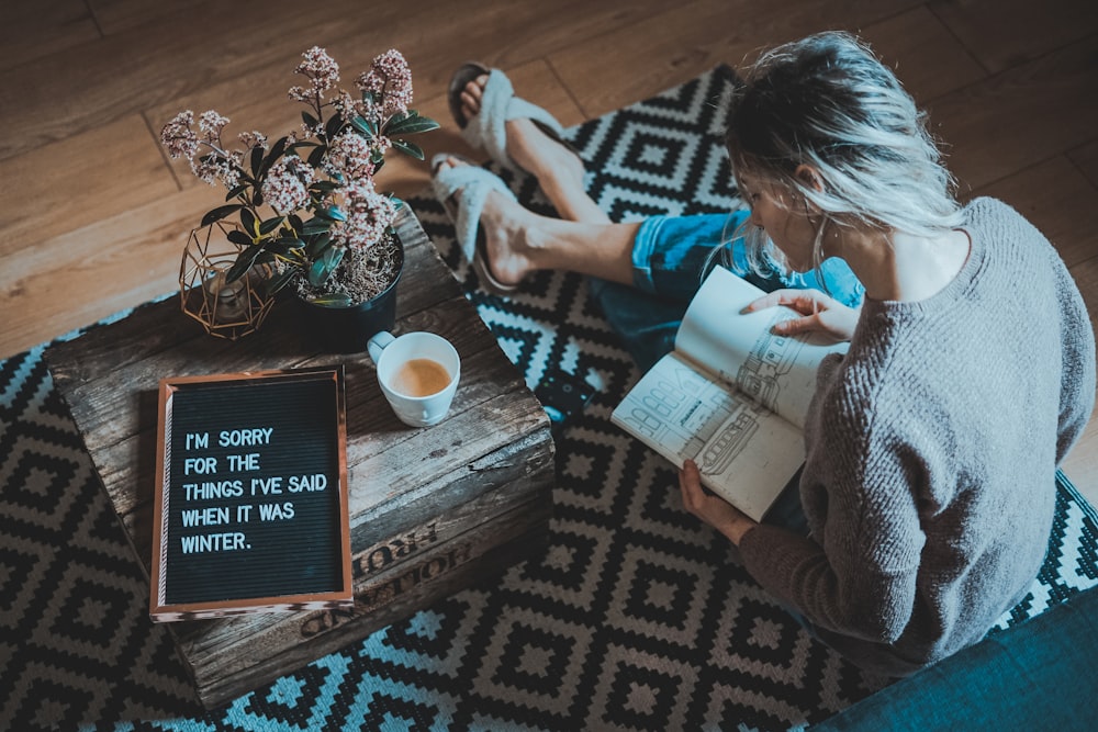 커피 테이블 근처에서 책을 읽는 동안 양탄자에 앉아있는 여자