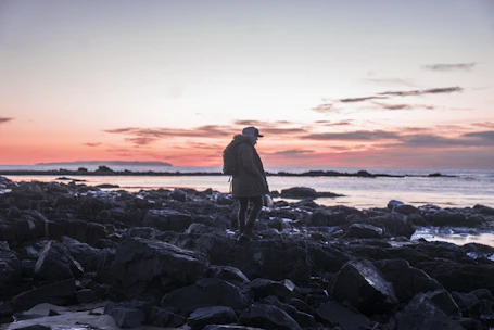 A traveler with a backpack hiking along a scenic Mediterranean trail at sunset.