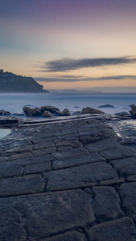 A misty Atlantic coastline at dawn with soft natural light illuminating the rugged shore.