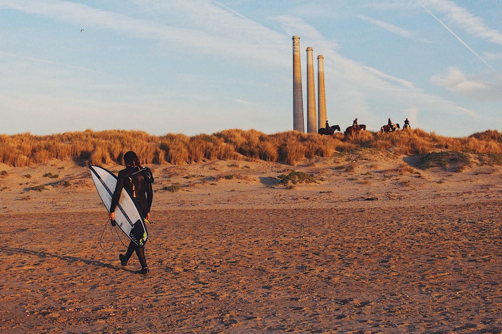 person carrying surfboard on sand