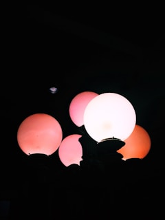 A cluster of glowing, spherical street lamps with a mix of white and pinkish hues illuminated against a dark background. The lamps are arranged closely together, creating a warm and ambient glow.