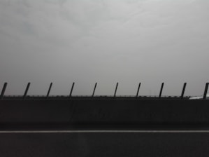 A road with a concrete barrier featuring upright posts, set against a hazy and overcast sky.