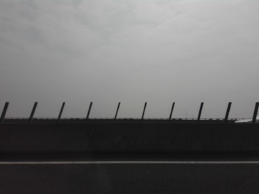 A road with a concrete barrier featuring upright posts, set against a hazy and overcast sky.