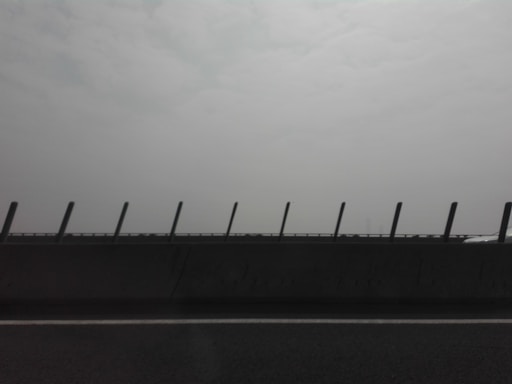A road with a concrete barrier featuring upright posts, set against a hazy and overcast sky.