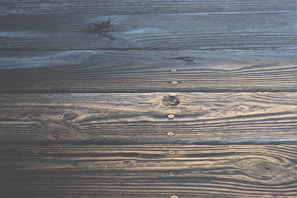 Weathered wooden planks aligned horizontally, showcasing distinct grain patterns and knots. Metal screws are visible at regular intervals along the slats.