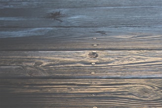 Weathered wooden planks aligned horizontally, showcasing distinct grain patterns and knots. Metal screws are visible at regular intervals along the slats.