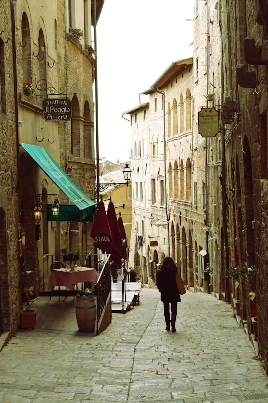 woman in black coat walking on sidewalk during daytime in Volterra Italy