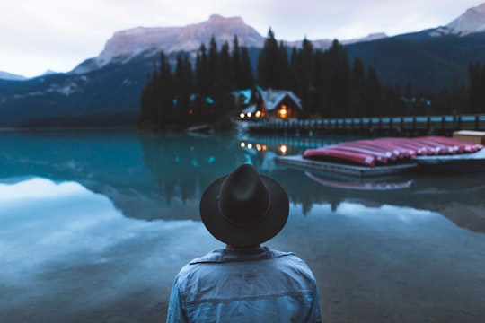 man standing infront of water with boats on dock with house nearby in Emerald Lake Lodge Canada