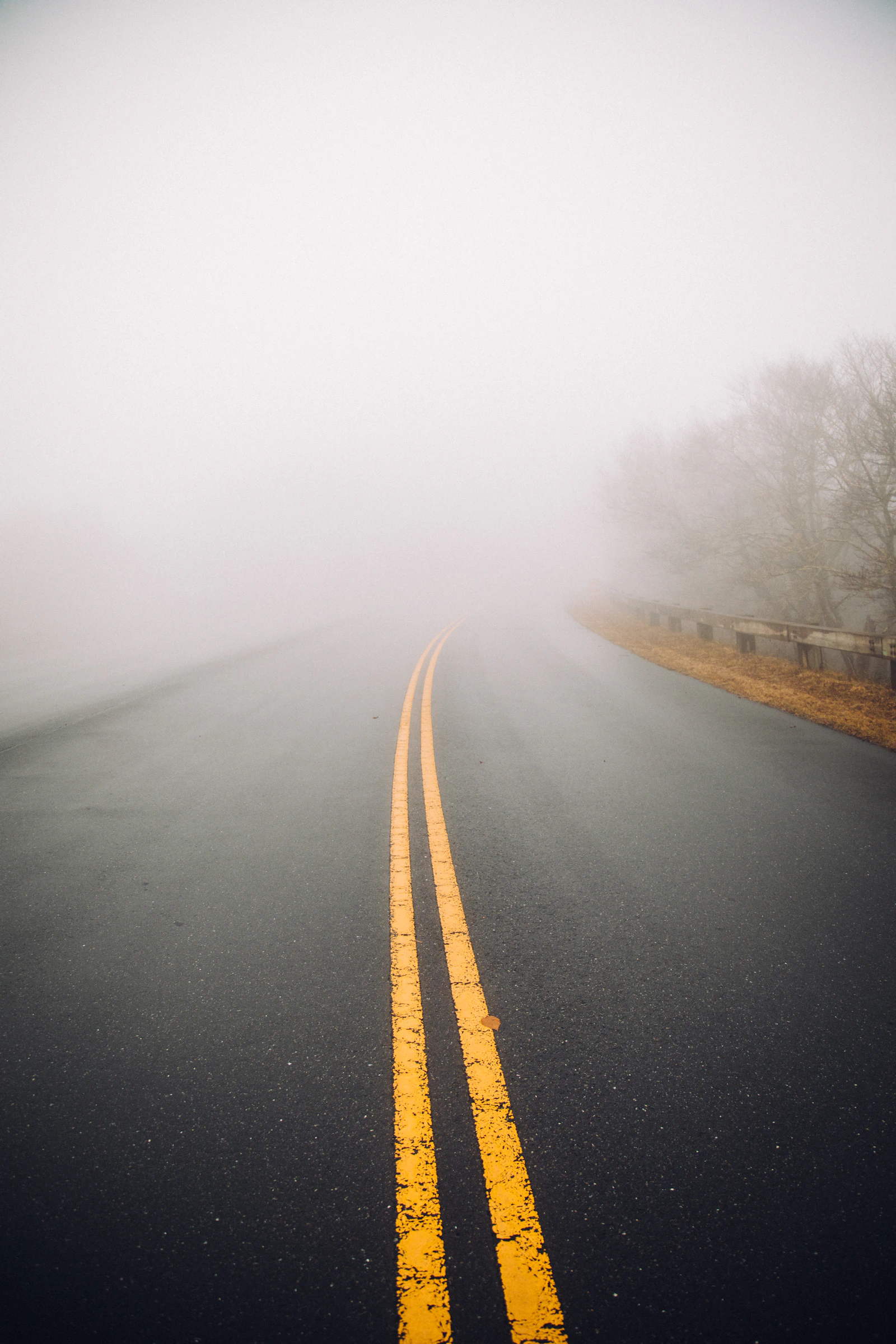 An empty two-lane road disappearing into morning fog