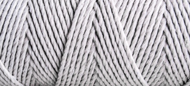 Close-up view of tightly wound, light gray yarn with visible texture and patterns formed by the twisted strands.