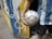 A person wearing a blue and white striped jersey is holding a soccer ball wrapped in plastic. The scene is set against a vibrant mural with swirling patterns in blue, yellow, and white. The setting appears to be outdoors, possibly near a street or alley.