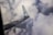 A view of an airplane wing with a logo against a backdrop of dense, fluffy clouds.