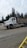 A large white construction truck is parked on a gravel area with trees in the background under an overcast sky.