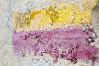 Peeling layers of paint in vibrant shades of yellow and pink create a textured and weathered surface on a wall.