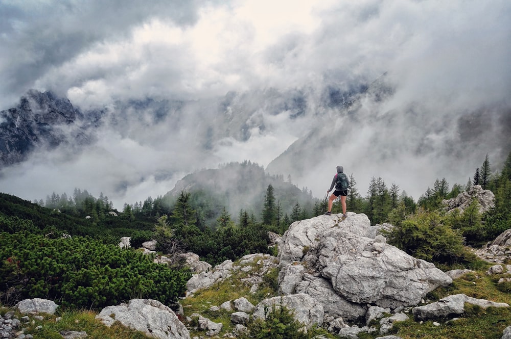 person standing on gray boulder looking at mountains