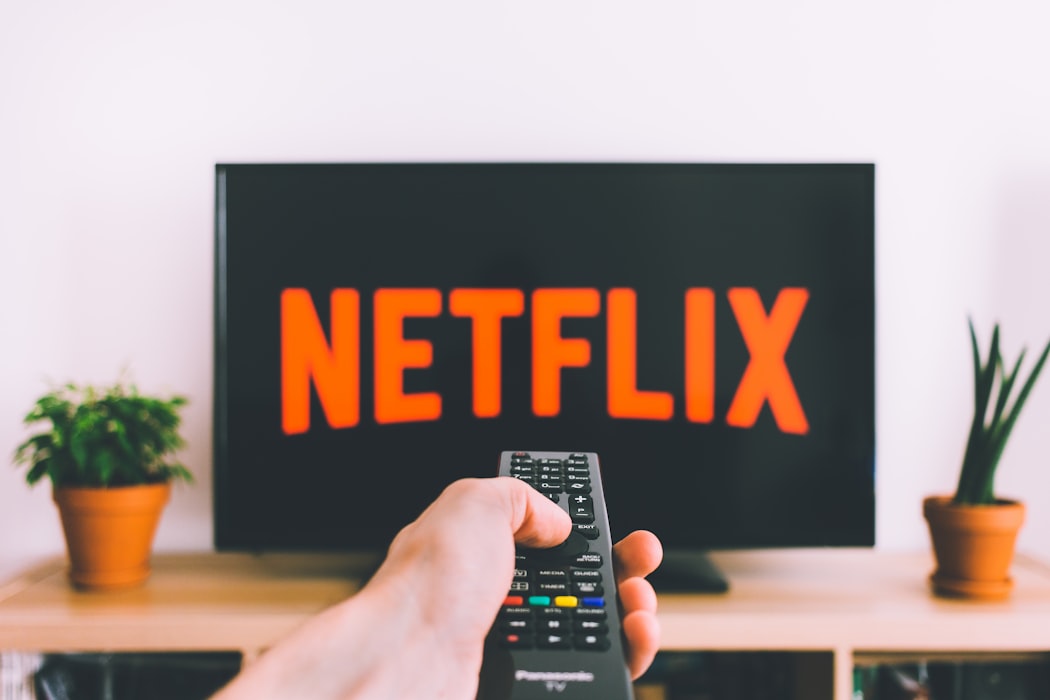A person holding a TV remote in front of their TV with Netflix.