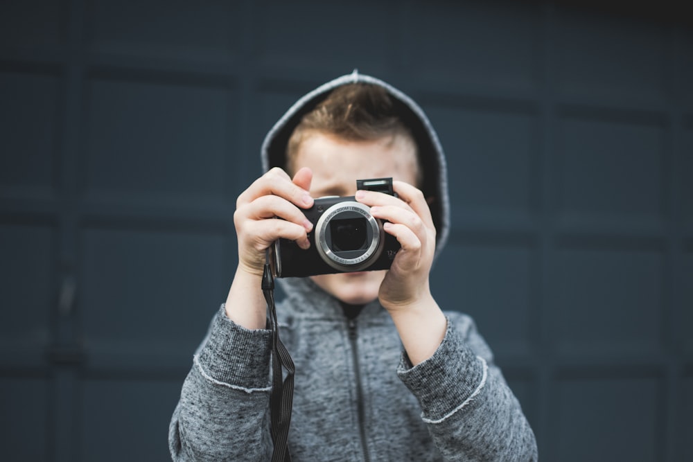 person in grey hoodie holding up camera over face