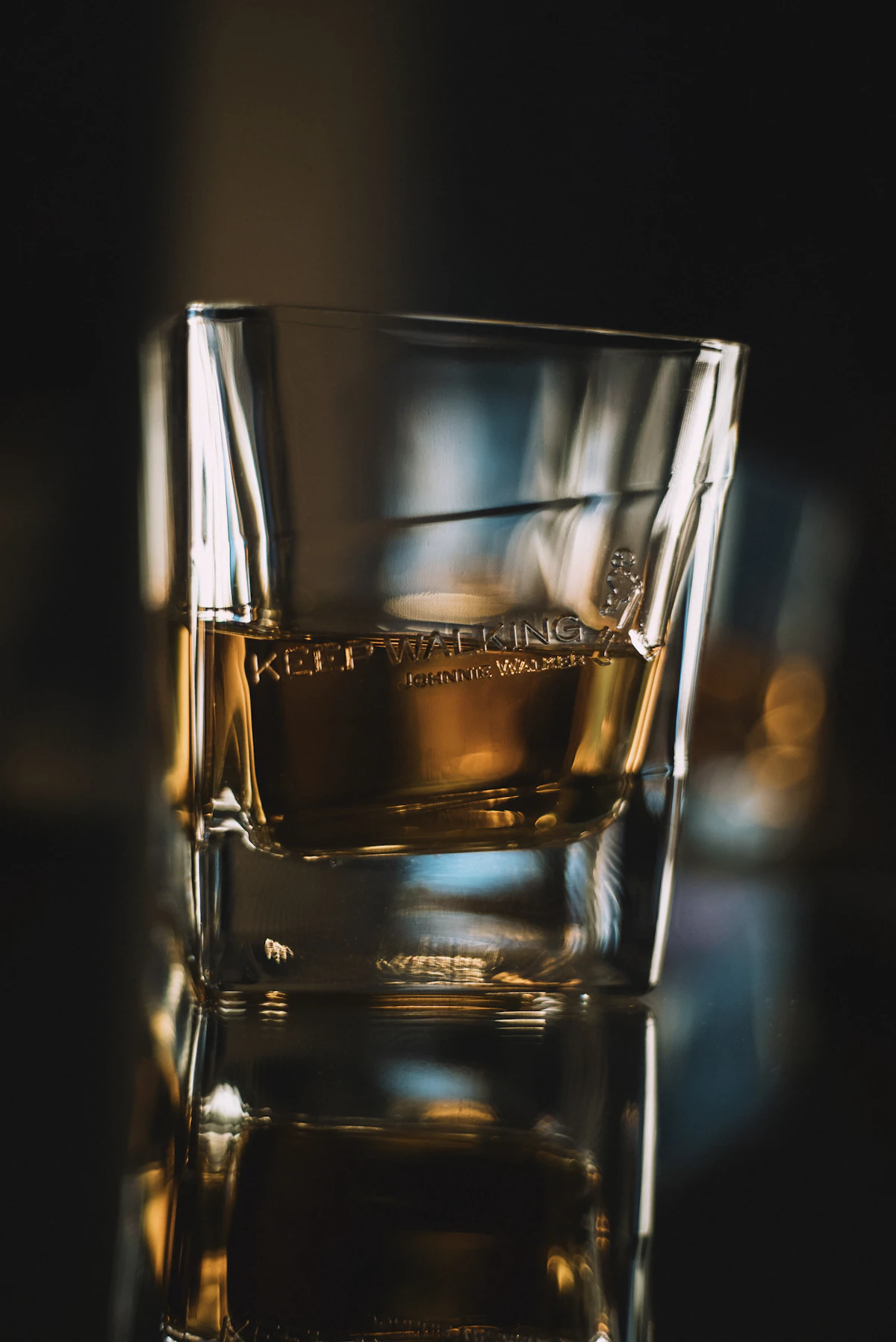 Whisky tumbler with neat pour on a dark mahogany surface.