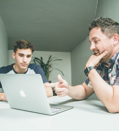 man wearing white and black plaid button-up sports shirt pointing the silver MacBook