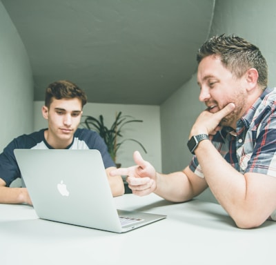 man wearing white and black plaid button-up sports shirt pointing the silver MacBook