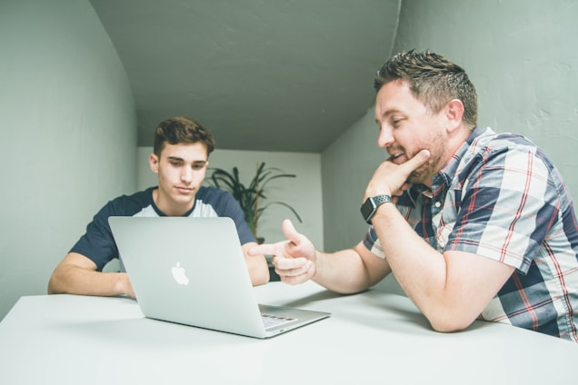 A mentor and protege engaged in a focused discussion with a laptop and notes in a cozy learning space.