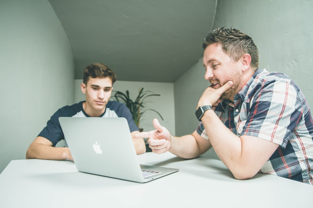 man wearing white and black plaid button-up sports shirt pointing the silver MacBook