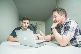 Dois homens conversando numa mesa com um computador