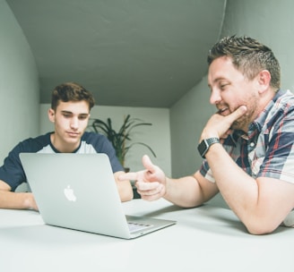 man wearing white and black plaid button-up sports shirt pointing the silver MacBook