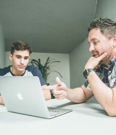 man wearing white and black plaid button-up sports shirt pointing the silver MacBook