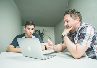 man wearing white and black plaid button-up sports shirt pointing the silver MacBook