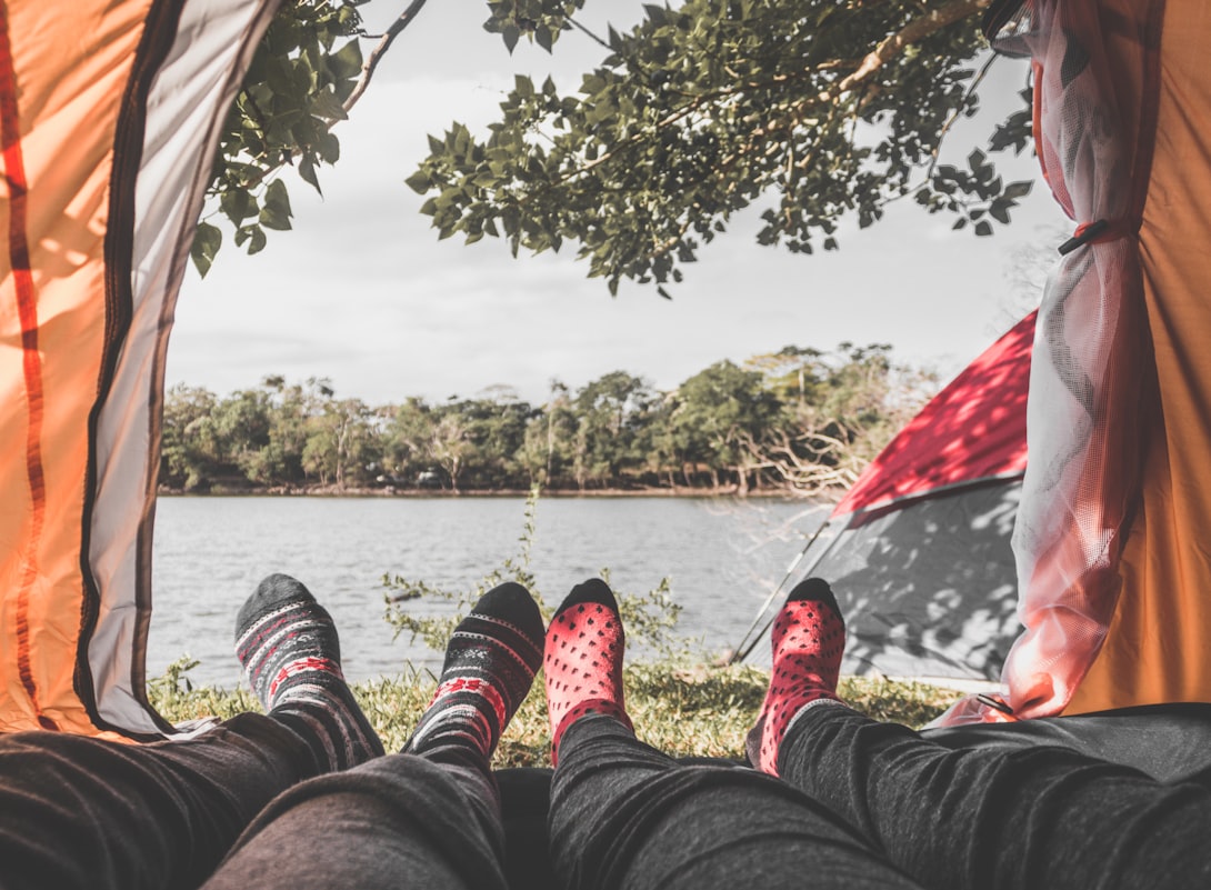 Image is of feet hanging out in the doorway of a tent looking out towards a body of water