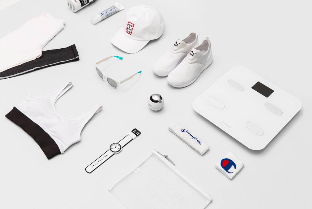Flat lay of sneakers, sunglasses, a cap, leggings, and a sports bra on a plain surface