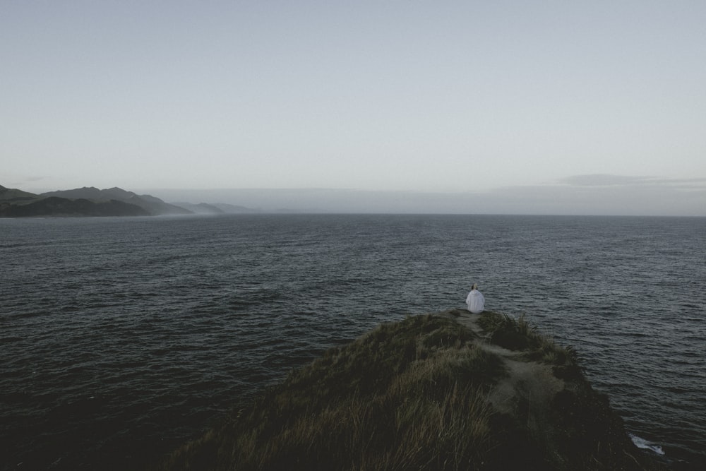 person sitting on a cliff beside a body of water